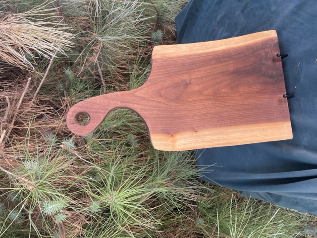 A black walnut charcuterie board with a curved handle.